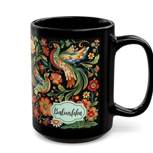 May include: Black ceramic mug with a colorful floral and bird design. The design features a green, yellow, and red bird with a green, yellow, and red floral pattern. The mug has the word "Babushka" written on it.