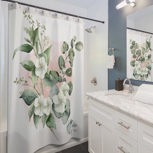 May include: White floral shower curtain with green leaves and a pink watercolor background. The curtain is hanging in a bathroom with a white vanity and a mirror.
