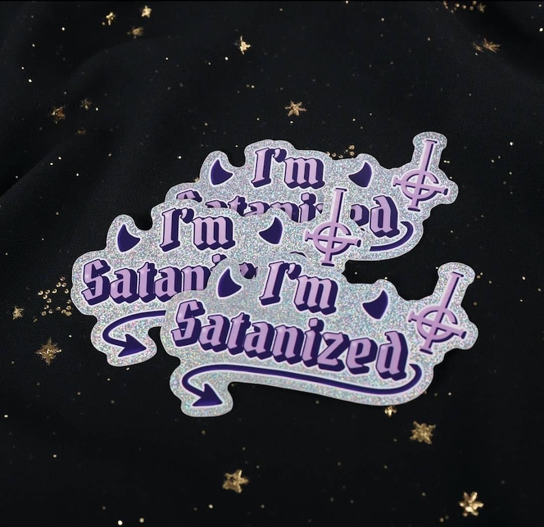 May include: A set of glittery stickers with the text "I'm Satanized" in purple and white. The stickers feature a stylized cross symbol and are set against a dark background with star-shaped sparkles.