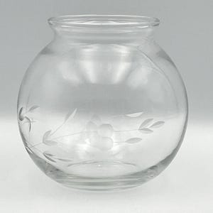 May include: A clear glass vase with a round body and a wide opening. The vase features etched floral and leaf designs. The glass is transparent, allowing light to pass through. This decorative vase is suitable for displaying flowers or as a standalone accent piece.