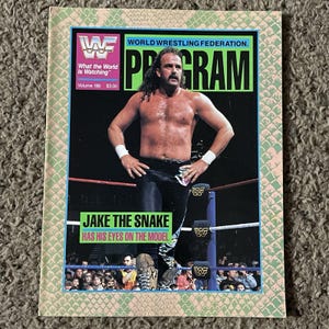 Puede incluir: Un programa vintage de la WWF World Wrestling Federation, volumen 189, con Jake the Snake en la portada. La portada muestra el texto What the World Is Watching, Program, y Jake the Snake Has His Eyes on the Model, con un borde de piel de serpiente.