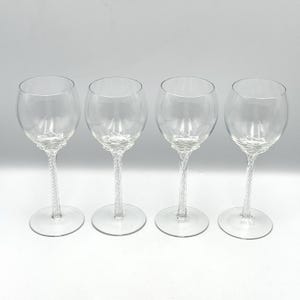May include: A set of four clear glass wine glasses, each featuring a rounded bowl and a distinctive twisted stem design. The glasses have a circular base and a smooth, transparent finish, showcasing a uniform construction across all four pieces.