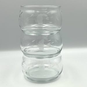 May include: Three clear glass bowls stacked on top of each other. Each bowl has a rounded shape and is decorated with an etched floral design. The bowls are transparent, allowing a clear view through them.