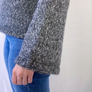 May include: A gray and white speckled sweater with long sleeves and a ribbed hem.