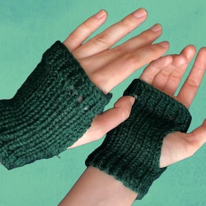 Könnte beinhalten: Dunkelgrüne gestrickte Fingerhandschuhe. Die Handschuhe sind aus einem strukturierten Garn gefertigt und haben eine gerippte Manschette und ein Loch für den Daumen. Der Hintergrund ist einfarbig türkis.