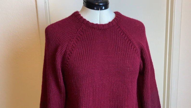 May include: A maroon knitted sweater with a crew neck and long sleeves.