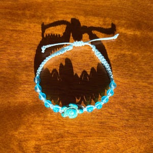 May include: A light blue friendship bracelet with a turquoise turtle charm and blue glass beads.