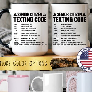 May include: White ceramic mugs with black handles and rims, printed with "SENIOR CITIZEN TEXTING CODE" and a list of acronyms and their meanings. Additional mugs in pink and white are shown below. Made in USA.