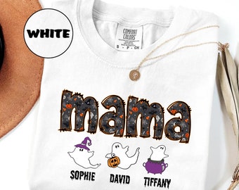May include: White Comfort Colors t-shirt with the word "mama" in a black and orange Halloween-themed design. Below the word "mama" are three cartoon ghosts with the names Sophie, David, and Tiffany. A gold necklace is draped over the shirt.