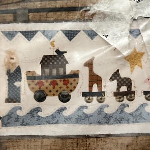 May include: A fabric panel featuring a whimsical Noah's Ark design. The ark is depicted as a train car with heart and dot patterns, accompanied by animal train cars. The design includes a blue wave border and a starry night sky.