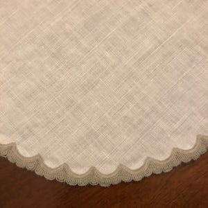 May include: A white linen table runner with a scalloped edge and a gray trim.
