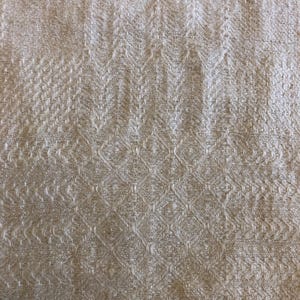 May include: Close-up of a beige textile with a woven pattern. The fabric has a textured surface with a repeating diamond and chevron design. The neutral color and detailed weave suggest a natural fiber material.