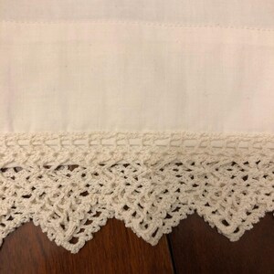May include: White cotton fabric with a crocheted lace trim. The lace is a delicate pattern with a scalloped edge.