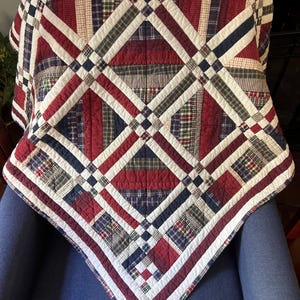 May include: A patchwork quilt with a geometric design in red, white, and navy blue. The quilt is draped over a blue chair. The quilt features a variety of plaid and solid fabric squares.