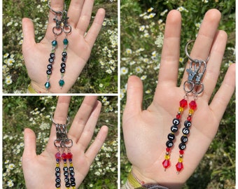 May include: Three beaded keychains with black letter beads and colorful crystal beads. The keychains spell out "GR83", "LM44", "SP11", "MV01", "DRO03", "CS55", and "CL16".