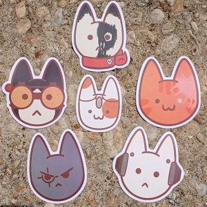May include: Six colorful cat stickers with different expressions and designs. The stickers are on a brown and white textured surface.