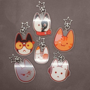 Pode incluir: Cinco chaveiros coloridos em forma de gato com pingentes em forma de estrela. Cada chaveiro apresenta um design de gato diferente com expressões faciais e detalhes únicos.