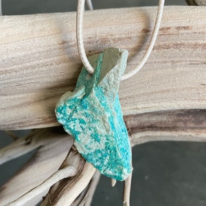 May include: A turquoise and white stone pendant on a white cord necklace. The stone is irregularly shaped and has a rough texture.