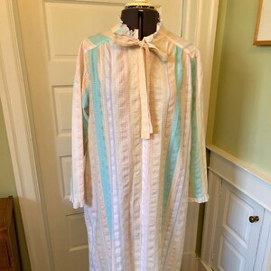 May include: A long, striped nightgown with a pink, white, and blue color scheme. The gown has a ruffled collar and a tie at the neck.