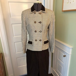 May include: A black and white checkered blazer with a black collar and brown trim. The blazer has a double breasted closure with gold buttons. The blazer is paired with black pants.