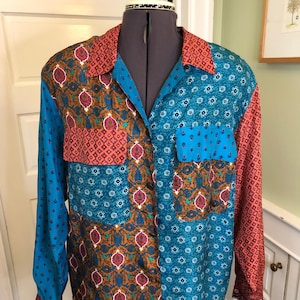 May include: A patchwork long-sleeved shirt with a button-down front. The shirt combines teal, orange, and brown patterned fabrics. The collar and cuffs are orange with a geometric design, and the body has floral and paisley patterns.