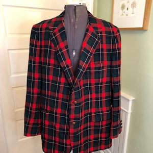 May include: A red, green, and navy plaid blazer with two brown buttons. The blazer is displayed on a mannequin. The jacket has two front pockets and a notched lapel. The plaid pattern is a classic design.