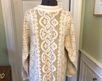 May include: Cream-colored sweater with a gold and white patterned design. The sweater features a geometric and floral pattern, long sleeves, and a crew neck. The sweater is displayed on a mannequin.