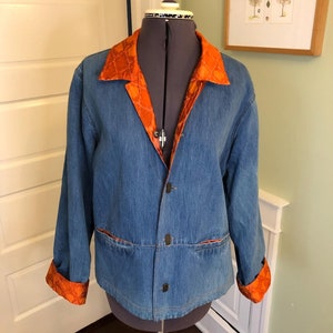 Puede incluir: Una chaqueta vaquera azul con un forro contrastante de color naranja y marrón con estampado en el cuello y los puños.