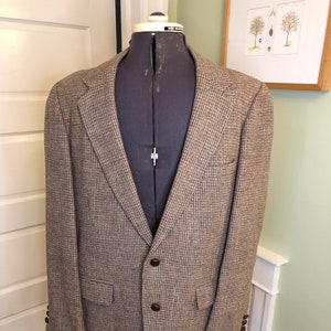 May include: A brown and tan tweed blazer with a classic two-button closure and notched lapels. The blazer features a subtle plaid pattern, two front pockets, and buttoned cuffs. The jacket is displayed on a mannequin.
