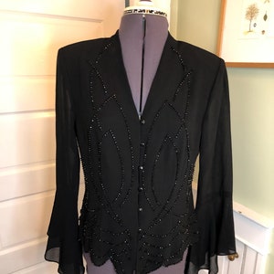 May include: A black long-sleeved blouse with a V-neckline and a beaded design. The blouse has a button-up front and bell sleeves.