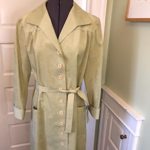 May include: A long-sleeved, light green dress with a button-up front and a matching belt. The dress has a collared neckline and two pockets.