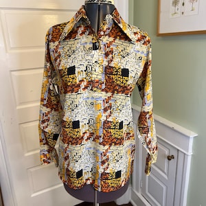 May include: A vintage button-down shirt with a bold, abstract pattern in shades of beige, brown, yellow, and black. The long-sleeved shirt is displayed on a mannequin, showcasing its wide collar and unique design. The shirt's pattern gives it a retro aesthetic.