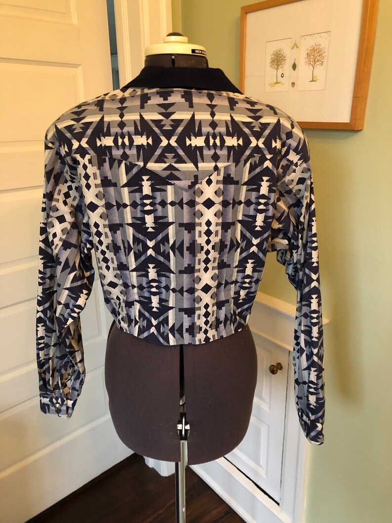 May include: A long-sleeved shirt with a geometric pattern in shades of blue, white, and gray. The shirt has a pointed collar and a button-up front.