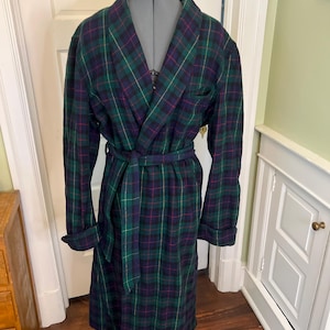 May include: A long-sleeved robe featuring a dark green, navy blue, and thin magenta plaid pattern. The garment includes a shawl collar, a matching fabric tie belt at the waist, and folded cuffs on the sleeves, displayed on a dress form mannequin.