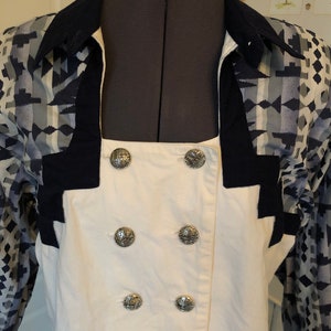 May include: A white button-up shirt with a double row of silver buttons. The shirt has a navy blue collar and cuffs with a geometric pattern in shades of blue and gray.