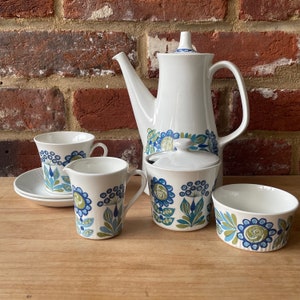May include: A white tea set with a blue and green floral pattern. The set includes a teapot, sugar bowl, creamer, and two cups and saucers.