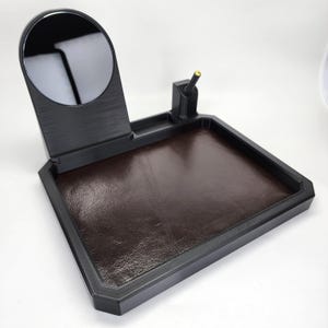 Pode incluir: Um organizador de mesa preto com um espelho embutido, um porta-canetas e uma bandeja de couro marrom.