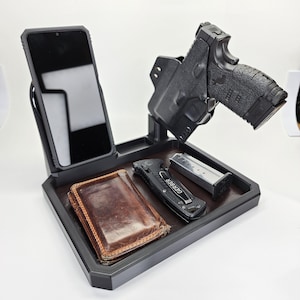May include: A black plastic tray with a phone holder, a gun holster, a wallet, a pocket knife, and a magazine. The tray is designed to hold everyday carry items.