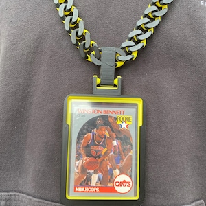 May include: A necklace with a basketball card pendant. The pendant is a Winston Bennett rookie card in a yellow and black frame. The chain is a chunky design with yellow, grey, and black links.