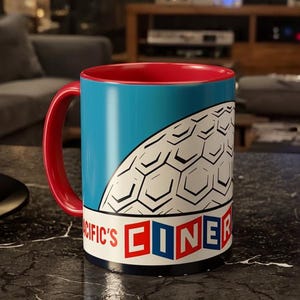 May include: A ceramic mug with a red interior and handle, and a blue exterior with a white and black geometric design. The mug has the words "PACIFIC'S CINER" in red and blue block letters.