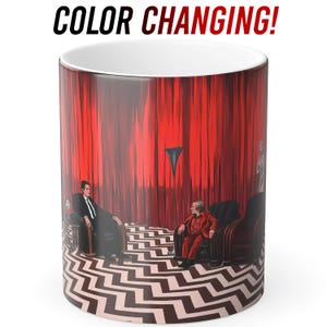 May include: A white ceramic colour-changing mug featuring a scene with red curtains, a black and white zigzag floor, and two figures in chairs. The mug has the text "COLOR CHANGING!" in black and red.