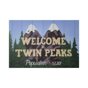 May include: A wooden sign featuring the words "WELCOME to TWIN PEAKS" in beige lettering, with a population count of 51,201. The sign depicts two mountain peaks with snow caps, set against a backdrop of green trees and a blue sky.