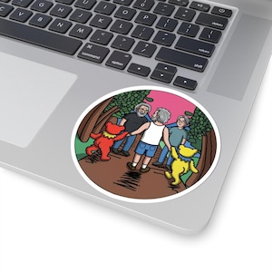 May include: A circular sticker showing an illustration of three men and two dancing bears in a forest setting. The bears are red and yellow, and the sky is pink. The sticker is on a laptop.