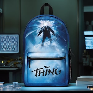 May include: Blue backpack with a graphic of a figure from the movie "The Thing" with the text "The Thing" printed on the front.