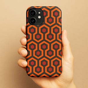 Puede incluir: Una funda de teléfono negra con un patrón geométrico repetido en naranja y rojo. El patrón se asemeja a la alfombra de la película "El Resplandor".