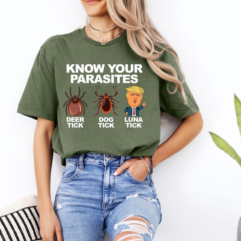 K&ouml;nnte beinhalten: Olivgr&uuml;nes T-Shirt mit dem Text "KNOW YOUR PARASITES" &uuml;ber Illustrationen einer Hirschzecke, Hundezecke und einer Cartoonfigur. Das Shirt ist aus einem weichen Material gefertigt.