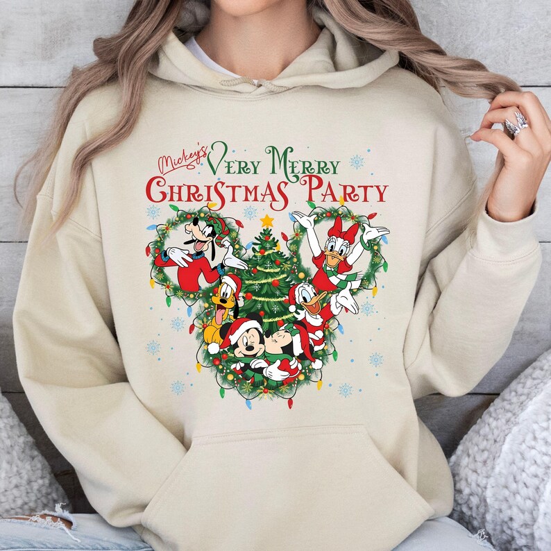 May include: Beige hoodie featuring a festive design. The graphic includes Mickey Mouse, Donald Duck, Goofy, and other Disney characters in a Christmas-themed arrangement. The text "Mickey's Very Merry Christmas Party" is displayed above the characters.