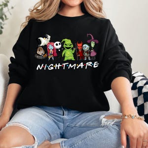 May include: Black sweatshirt featuring a colorful graphic of characters from "The Nightmare Before Christmas." The word "NIGHTMARE" is printed in white with colorful lights. The sweatshirt is a crew neck style.