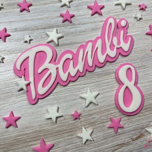May include: Pink and white fondant cake topper with the name "Bambi" and the number "8" surrounded by pink and white stars.