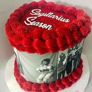 May include: A round cake with red frosting and the words "Sagittarius Season" in white. The cake is decorated with a red frosting border and a black and white photo wrap. The cake sits on a white cake board.